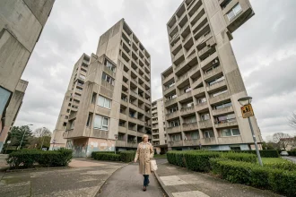 Vue en contre-plongée des tours de la Cité Pablo Picasso à Nanterre avec une passante sur le chemin piétonnier, architecture brutaliste en béton des années 1970